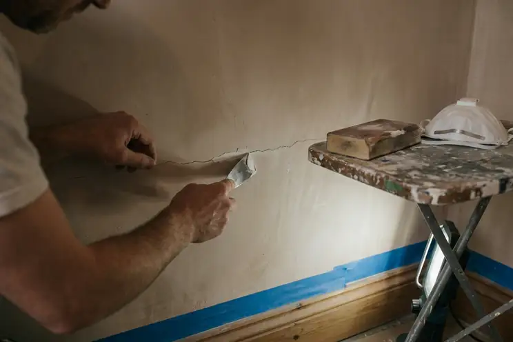 Peintre rebouchant une fissure au couteau à enduire avant ponçage sur un mur intérieur